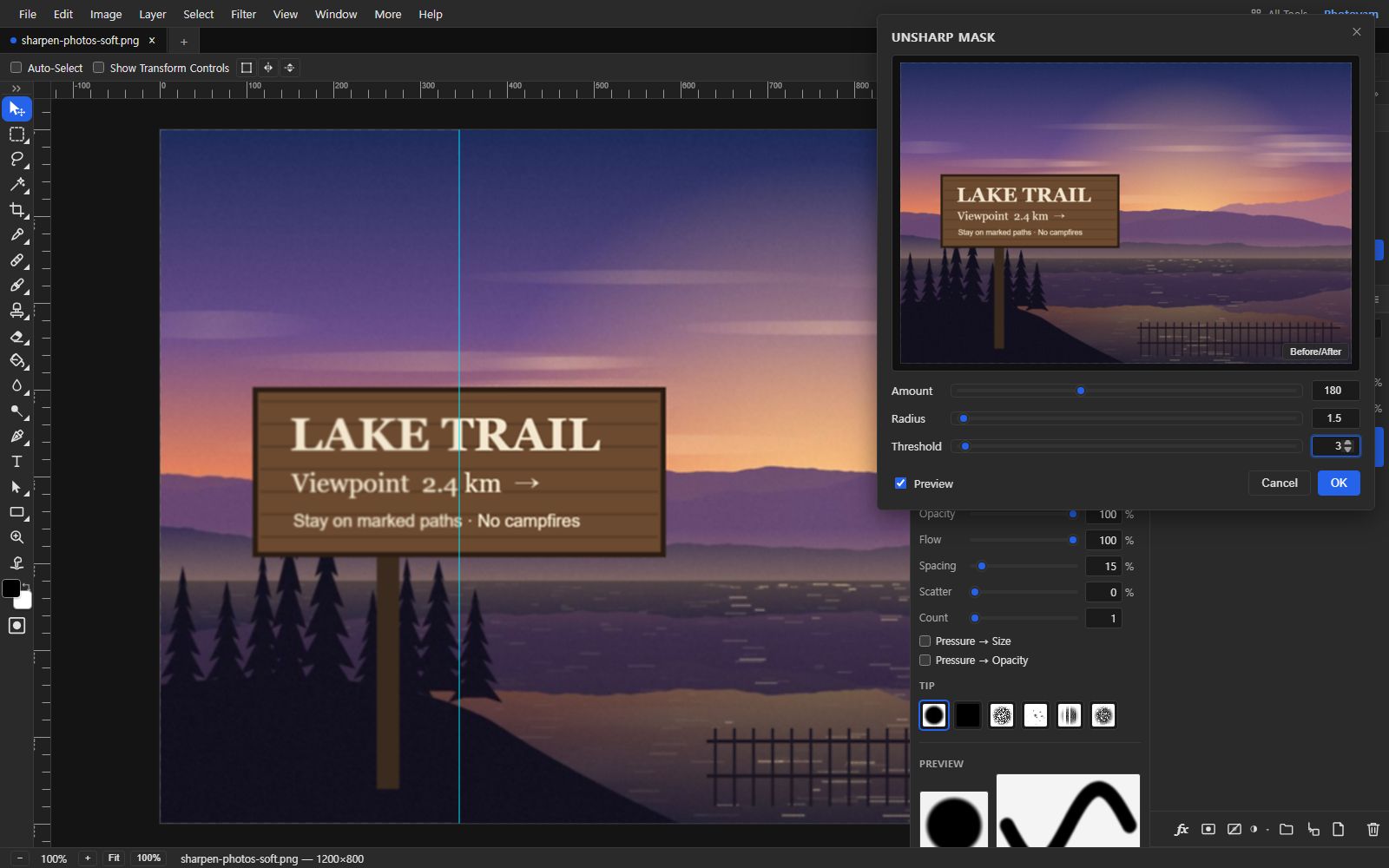 The Photoyam editor at 100% zoom on a soft illustration of a wooden trail sign reading LAKE TRAIL by a lake at sunset. A vertical guide splits the sign: the left half is soft, the right half is visibly crisper. The Unsharp Mask dialog is open with Amount 180, Radius 1.5 and Threshold 3, a live preview, and Cancel and OK buttons.